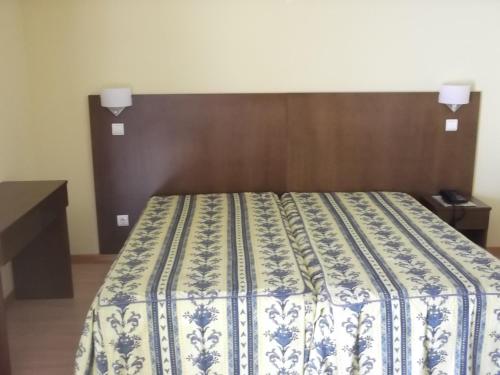a bed with a blue and white blanket on it at Hotel Minho Belo in Vila Nova de Cerveira