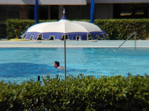 a man swimming in a swimming pool with an umbrella at Appartamenti Valbella con piscina in Bibione