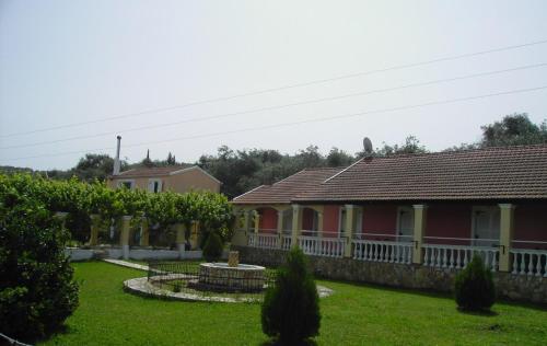 a red house with a white fence and a yard at Nikos Apartments in Acharavi
