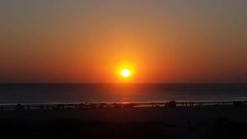 a sunset over the ocean with people walking on the beach at Apartamento Frente Mar in Arraial do Cabo