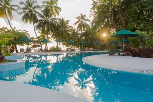 a swimming pool with palm trees and umbrellas at Equator Village Maldives in Gan
