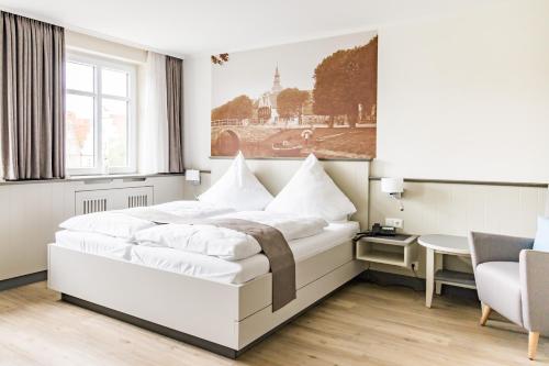 a white bedroom with a large bed and a table at Hotel Klein Amsterdam in Friedrichstadt