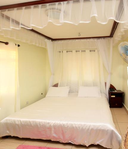 a bedroom with a white bed with white curtains at Scroll Inn Hotel in Kampala