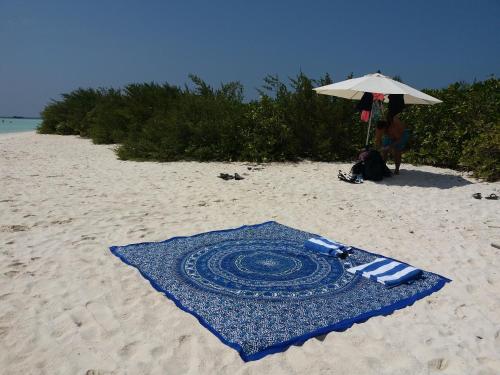 a blue rug on a sandy beach with an umbrella at Ras Rana Lodge in Rasdu