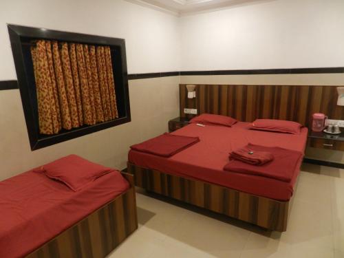 a bedroom with two beds with red sheets and a window at Sayeban Hotel in Matheran