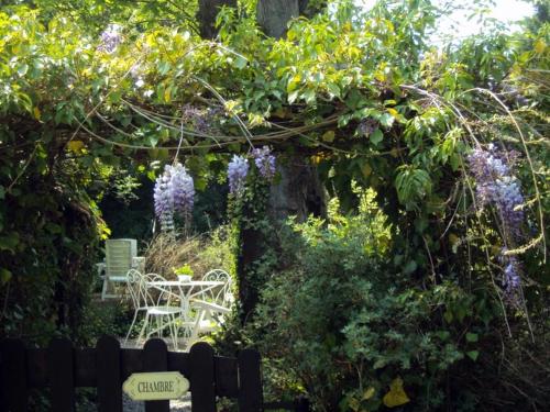 een tuin met een tafel en stoelen en paarse bloemen bij Chambre du Rouard LE RUISSEAU in Camiers