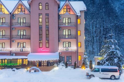 a large pink building with snow in front of it at Fantasia Hotel in Polyana