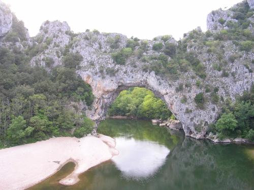 an arch in a river with trees and a beach at La Flor Azul in Grospierres