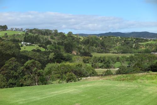 a green field with trees and mountains in the background at Kaka Lodge at Kotare House in Tawharanui