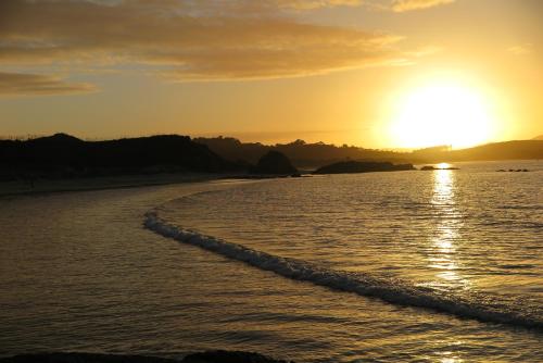 a sunset on a beach with the ocean at Kaka Lodge at Kotare House in Tawharanui
