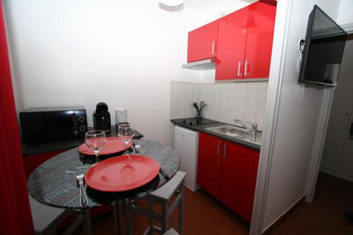 małą kuchnię z czerwonymi szafkami i stołem z kieliszkami do wina w obiekcie Studio Le Virgile - Annecy w Annecy