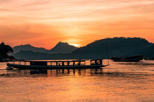 a boat floating on the water at sunset at Mekong Riverview Hotel in Luang Prabang