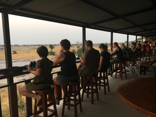 a group of people sitting at tables looking out at the savannah at Thobolo's Bush Lodge in Kachikau