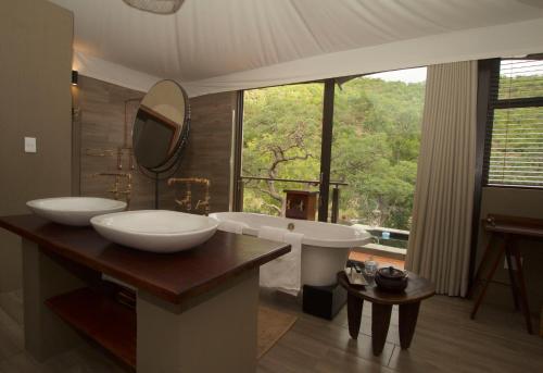 ein Badezimmer mit zwei Waschbecken, einer Badewanne und einem Fenster in der Unterkunft Inzalo Safari Lodge in Welgevonden Game Reserve