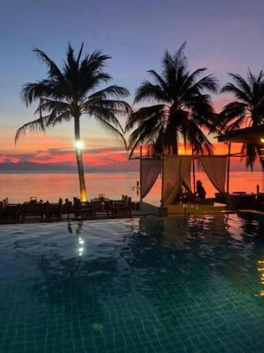 a swimming pool with palm trees and a sunset at Sun Beach Bungalows resort in Haad Rin