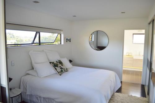a bedroom with a white bed and a mirror at Hahei Beach Apartment in Hahei