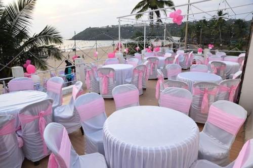 a bunch of tables and chairs with pink and white chairs at Saritas Guest House - Bogmalo Beach in Bogmolo