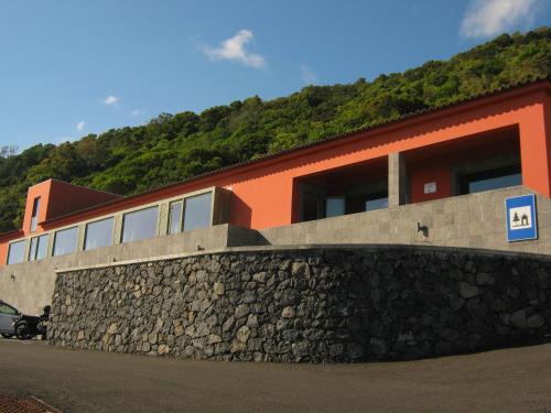 Azores Youth Hostels - São Jorge في Calheta: مبنى بحائط حجري بجانب تل