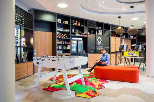 un homme assis sur un tabouret orange dans un magasin avec une table et une table dans l'établissement Aparthotel Adagio Köln City, à Cologne