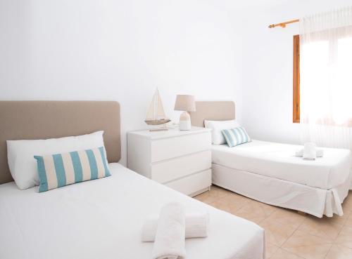 a white bedroom with two beds and a window at Villa Margarita in Es Mercadal