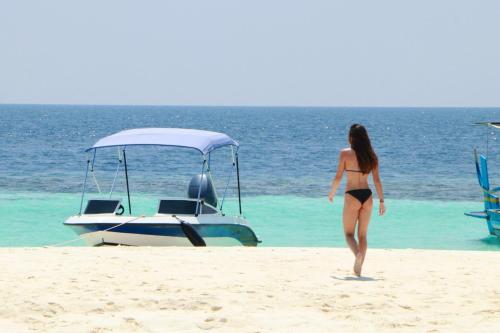 a woman walking on the beach next to a boat at By the shade Maldives in Hangnaameedhoo