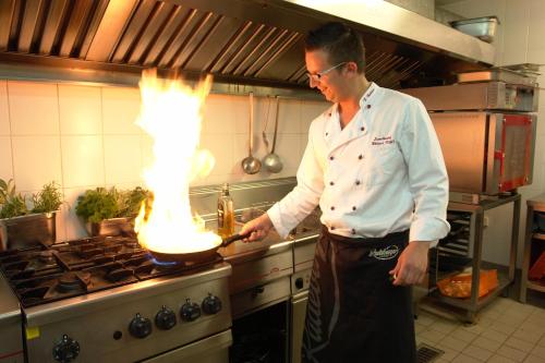 a man in a kitchen stirring a pot on a stove at Landhotel Weisses Röß`l in Adorf