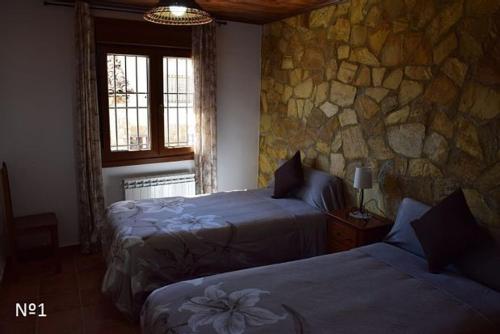 1 dormitorio con 2 camas y pared de piedra en Los Ayales, en Huelamos