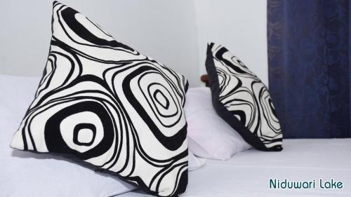a bed with black and white pillows on it at Niduwari Lake Homestay in Dambulla