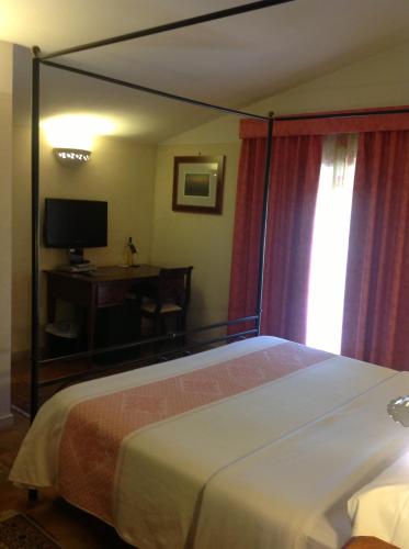 a bedroom with a bed and a desk and a television at Villa Acquaviva Wine Resort in Montemerano