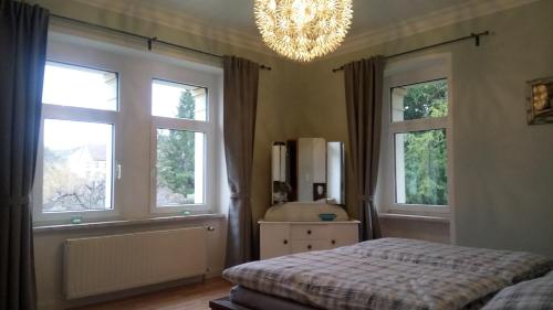 1 Schlafzimmer mit einem Bett, 2 Fenstern und einem Kronleuchter in der Unterkunft Villa Heimburg in Thale