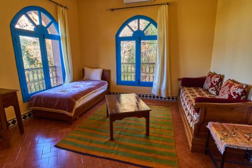 a living room with a bed and a couch and windows at Maison D'hotes Sahara in Aoufous