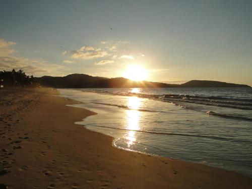 a beach with the sun setting on the water at Paraiso del Pescador in Rincon de Guayabitos