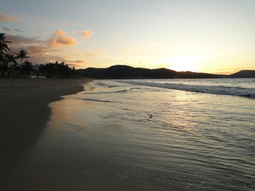 a beach with the sun setting over the ocean at Paraiso del Pescador in Rincon de Guayabitos