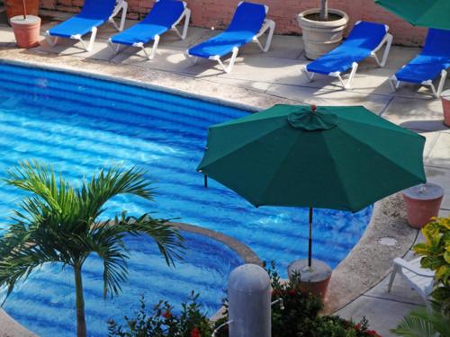 a pool with chairs and an umbrella next to a swimming pool at Paraiso del Pescador in Rincon de Guayabitos