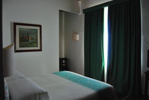 a bedroom with a bed and a window with green curtains at Villa Acquaviva Wine Resort in Montemerano