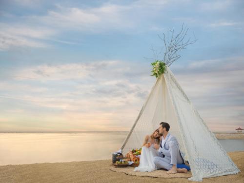 a bride and groom sitting in a teepee on the beach at Griya Santrian a Beach Resort And Spa in Sanur
