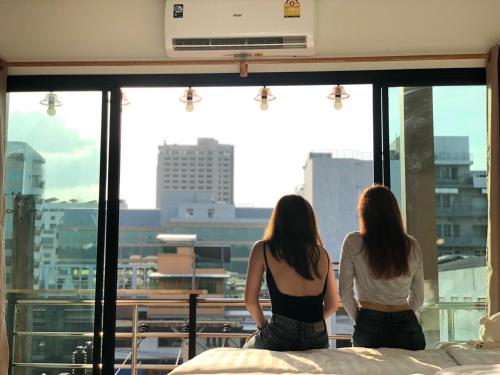 two women sitting on a bed looking out of a window at Khoksametchun Hostel in Hat Yai