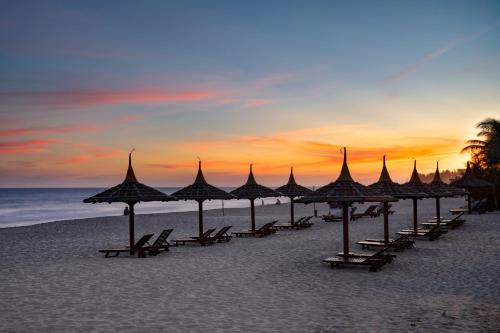 un gruppo di ombrelloni sulla spiaggia al tramonto di Terracotta Resort & Spa a Mui Ne