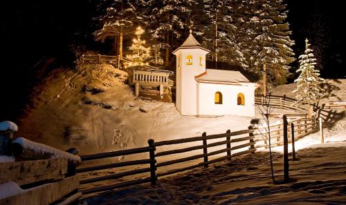 a small white church in the snow at night at Naturhotel Hüttenwirt im Grossarltal in Hüttschlag
