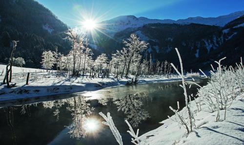 a river in the snow with the sun in the background at Naturhotel Hüttenwirt im Grossarltal in Hüttschlag