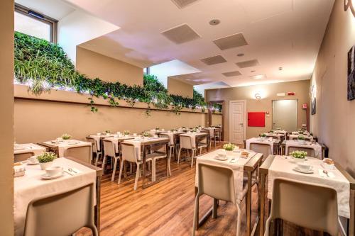 un restaurant avec des tables blanches, des chaises et des plantes dans l'établissement Al Manthia Hotel - Gruppo Trevi Hotels, à Rome