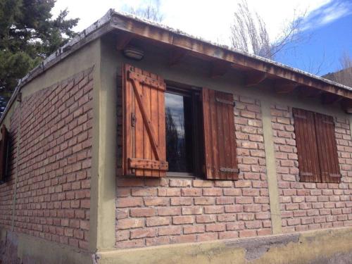a brick house with a window and wooden shutters at Cabaña de montaña in Potrerillos