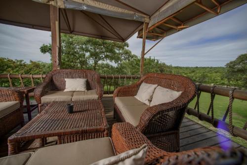 a deck with wicker chairs and a table and chairs at Nkambeni Safari Camp in Hazyview