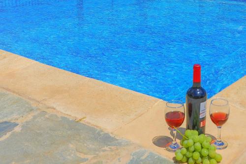 two glasses of wine and grapes next to a swimming pool at Villa Aphrodite Finiki in Polis Chrysochous