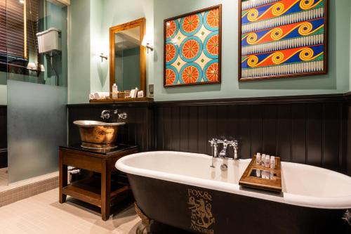 a bathroom with a tub and paintings on the wall at Fox and Anchor in London