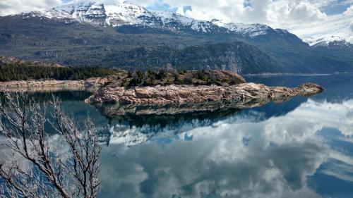 a small island in the middle of a lake with mountains at Cabañas Costa del Percy in Trevelin