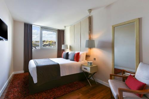 um quarto com uma cama, uma cadeira e um espelho em Fraser Place Canary Wharf em Londres