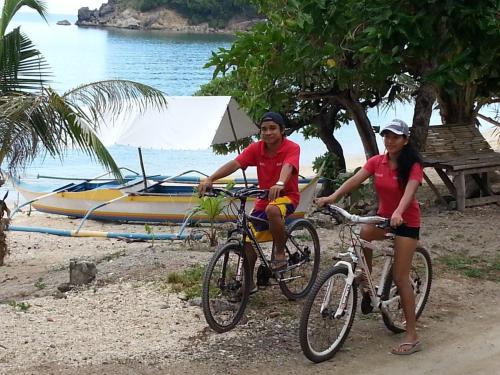 two people riding bikes on a beach with a boat at Binucot Beach Resort in Ferrol