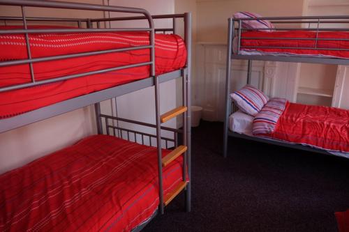 a room with three bunk beds with red sheets at Newbrough Bunkhouse in Hexham