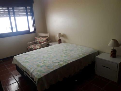 a bedroom with a bed and a chair and a window at Capão 2 Dormitorios in Capão da Canoa